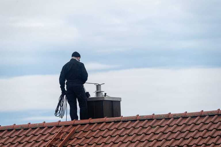 Schornsteinfeger auf Dach reinigt Kamin.
