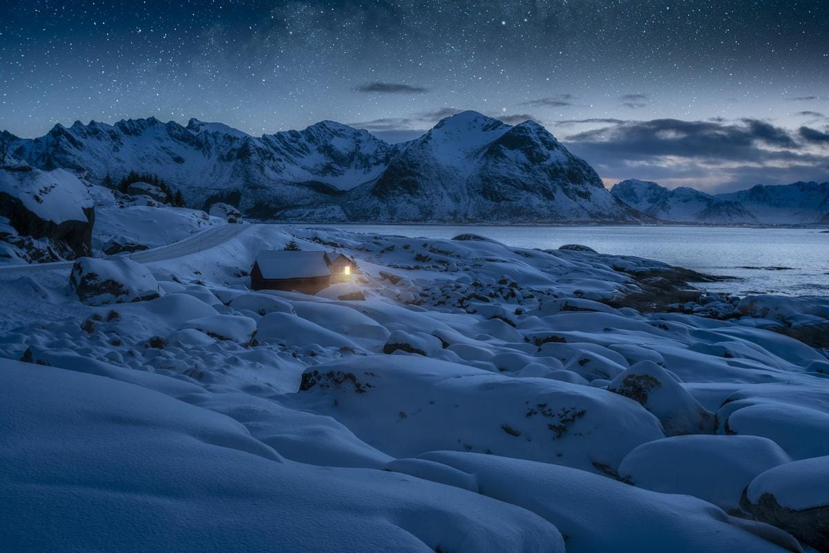 Tief verschneite nächtliche Winterlandschaft am Meer in Norwegen.