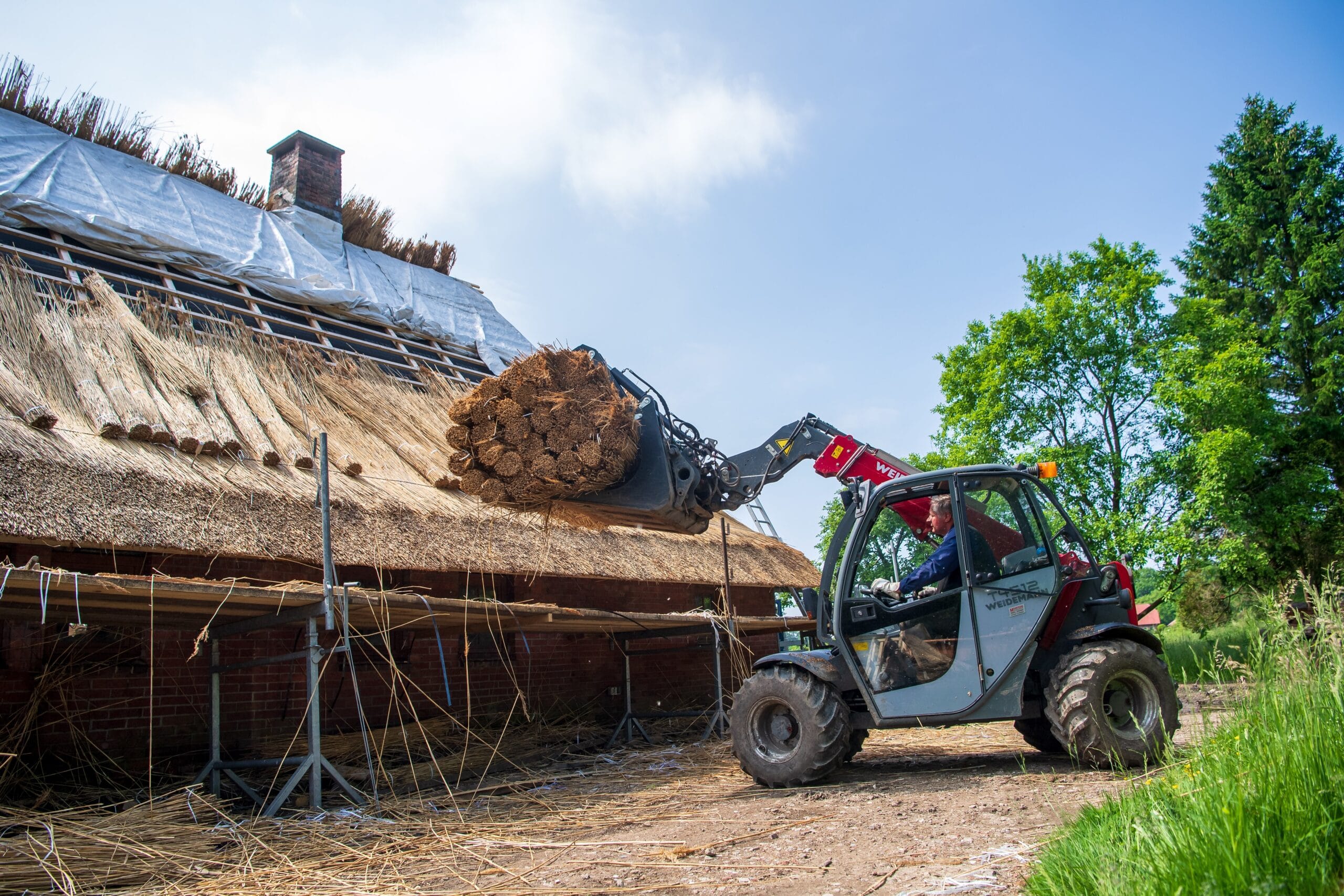 Bagger hebt Strohrollen auf ein zu deckendes Dach