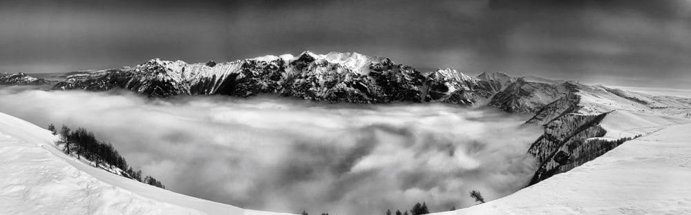Panorama-Aufnahme von einem Hochplateau von einer gegenüberliegenden Gipfelkette und einem von tiefstehenden Wolken verhangenen Tal