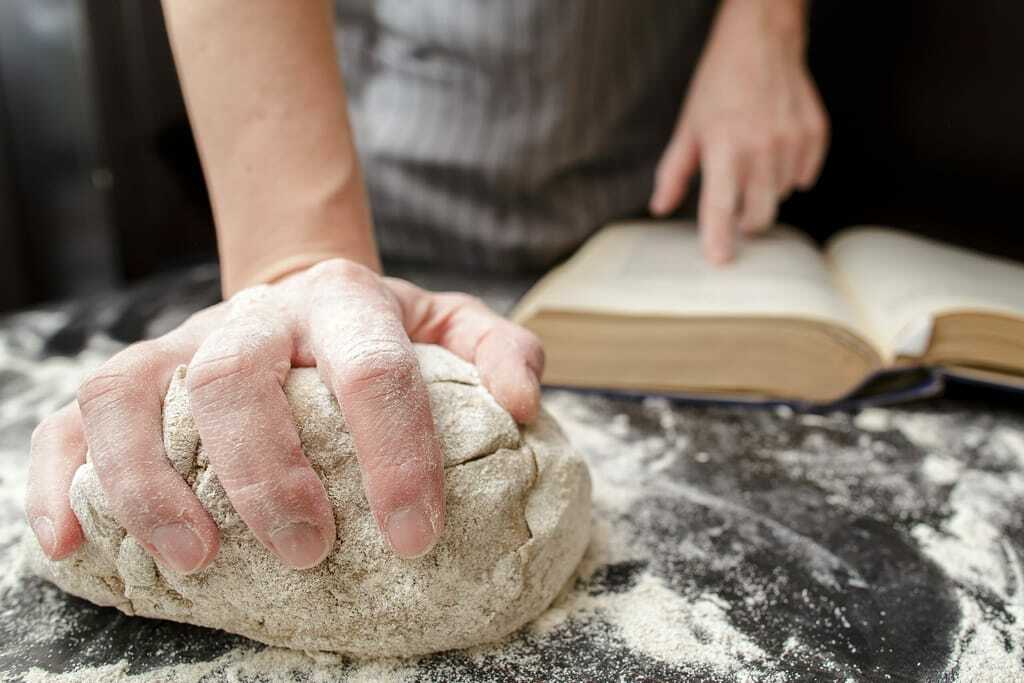 Bäcker knetet Brot und liest Handbuch.
