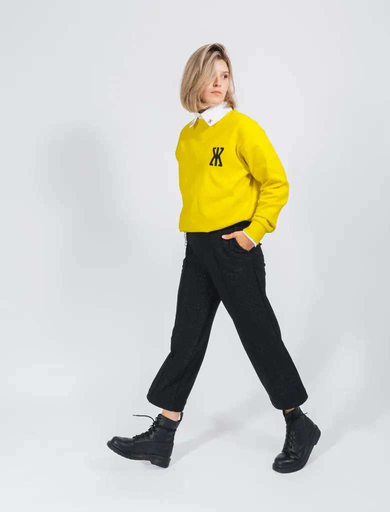 Model mit schwarzer Hose, neongelben Pulli und wei&szlig;em Hemd.