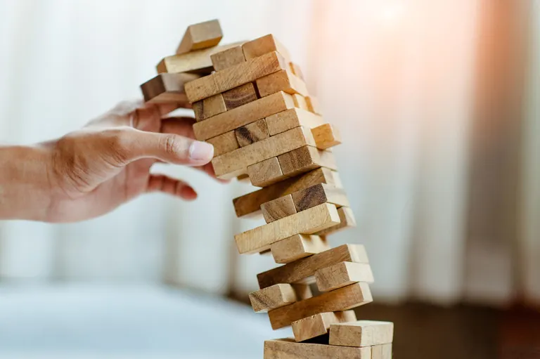Hand hält stürzenden Turm aus Bauklötzen.