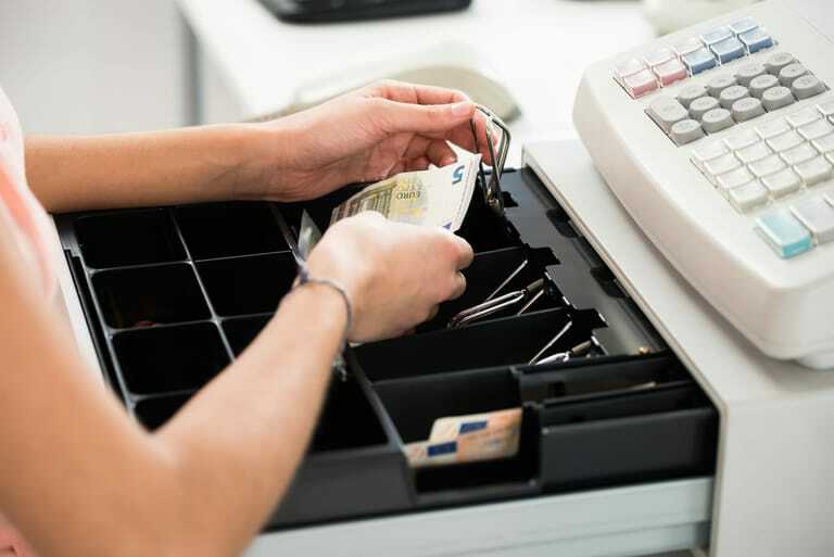Weibliche Hand legt Geldschein in Kasse.