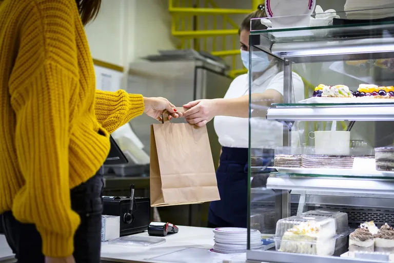 Verk&auml;uferin in B&auml;ckerei h&auml;ndigt Kundin T&uuml;te aus.