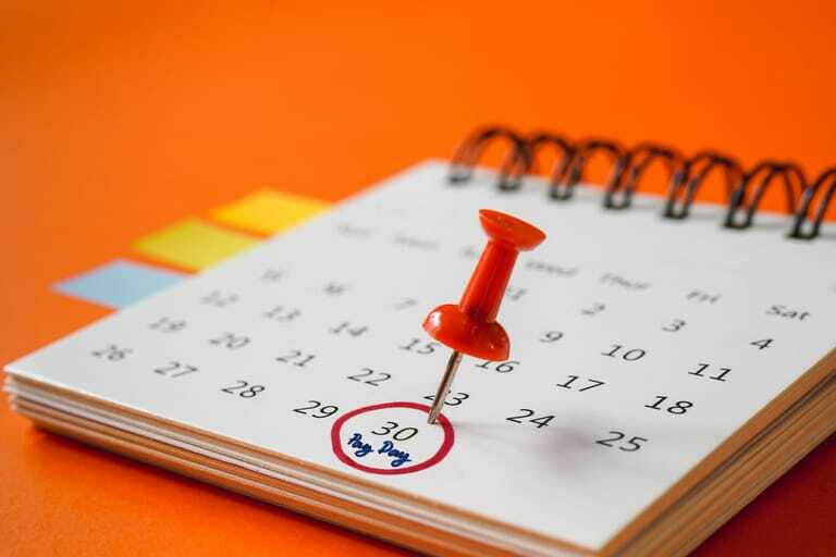 Kalender, in dem der Zahltag rot umkreist und angepinnt ist mit rotem Pin.