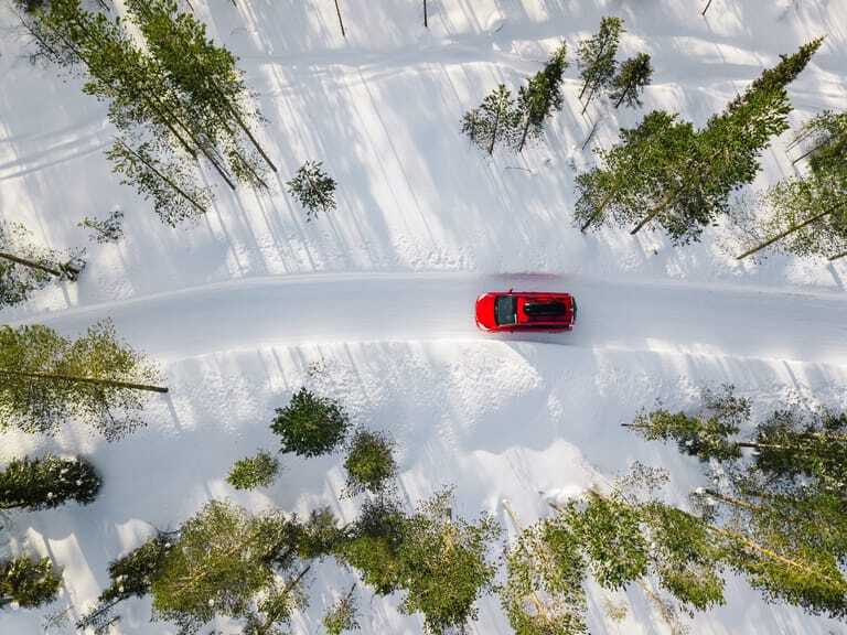Ein rotes Auto fährt durch eine Schneelandschaft.