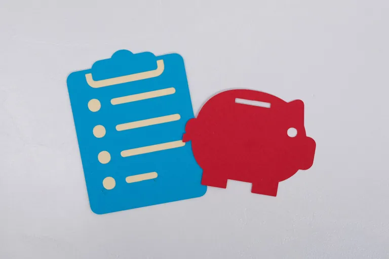 Klemmbrett und Sparschwin aus Papier auf weißem Hintergrund.