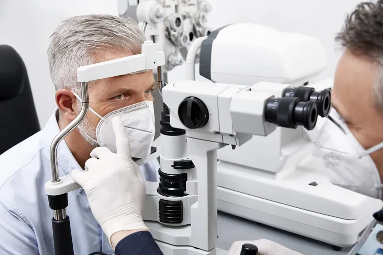 Augenoptiker zählen zu den Gesundheitshandwerken. Ein Augenoptiker untersucht Kunden mit FFP-2-Maske