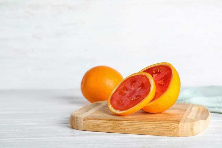 Holzbrett mit aufgeschnittener Orange, die innen eine Tomate enthüllt.