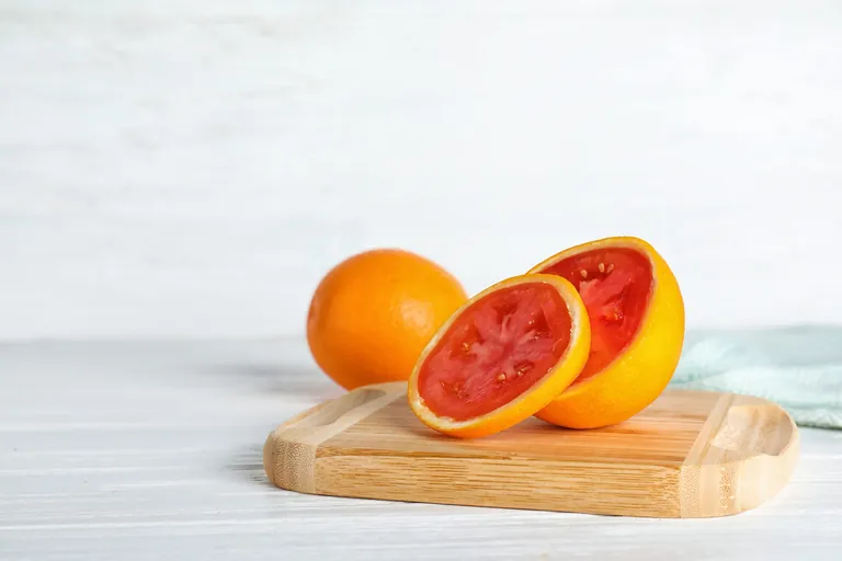 Holzbrett mit aufgeschnittener Orange, die innen eine Tomate enth&uuml;llt.