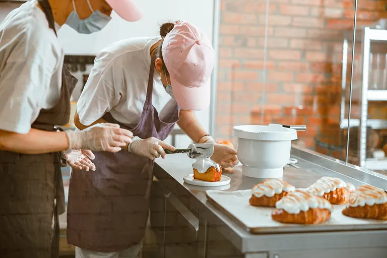 Ausbildung in der Kondtorei. Lehrling und Ausbilder dekorieren Backware mit Creme.