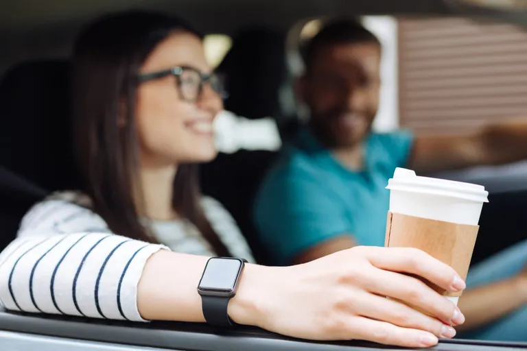 Frau und Mann in Auto, Frau hält Kaffeebecher aus Beifahrerfenster.