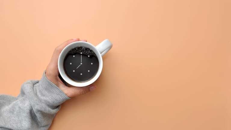 Hand h&auml;lt Kaffee mit Uhrensymbol.