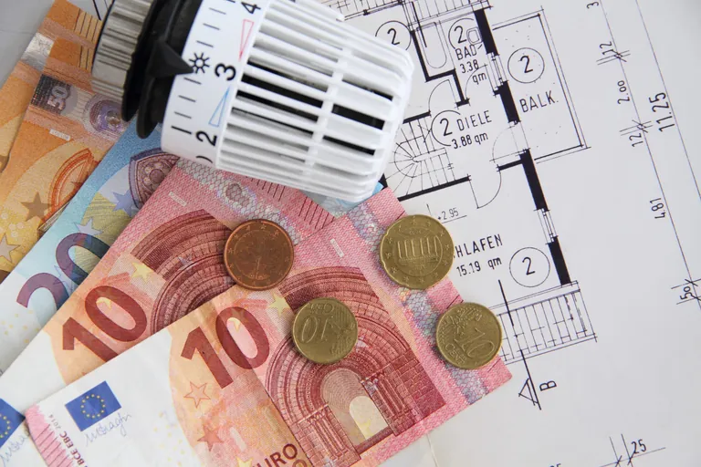 Heizungsthermostat mit Geldscheinen auf einem Bauplan.