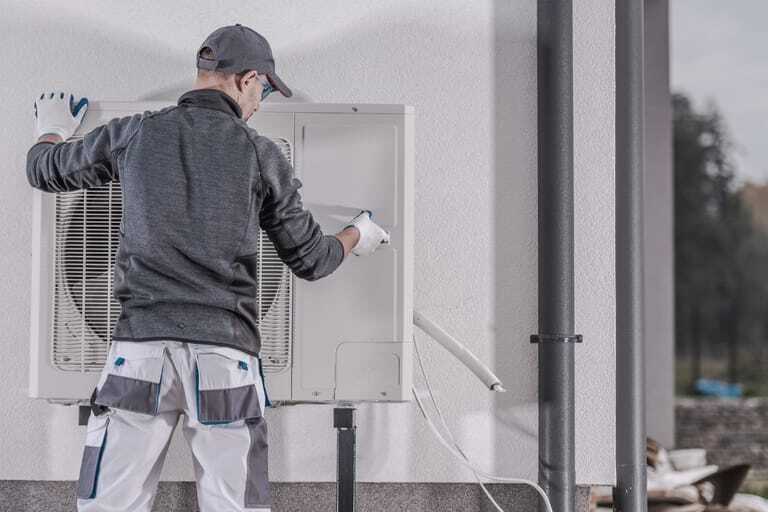Handwerker installiert Wärmepumpe an Wohnhaus.