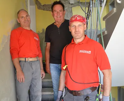 Hubert Schm&ouml;lz mit seinen beiden ukrainischen Mitarbeitern im Treppenhaus einer Baustelle