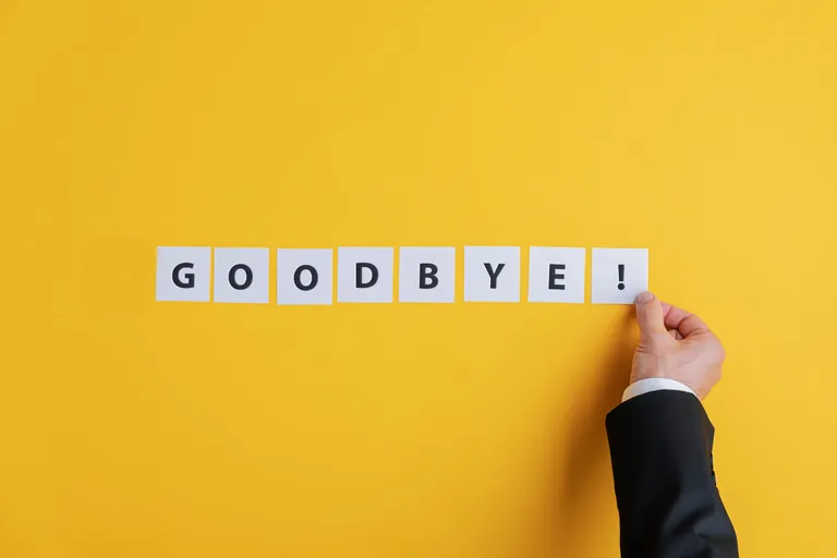 Hand legt Buchstaben zu Wort "Goodbye!" auf gelbem Hintergrund.