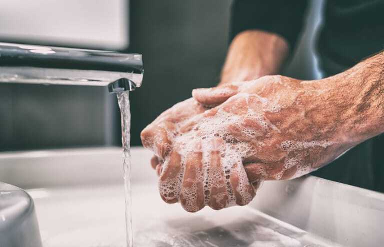 Mann seift Hände am Waschbecken ein.