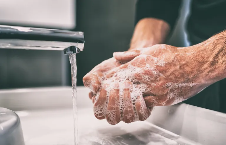 Mann seift Hände am Waschbecken ein.