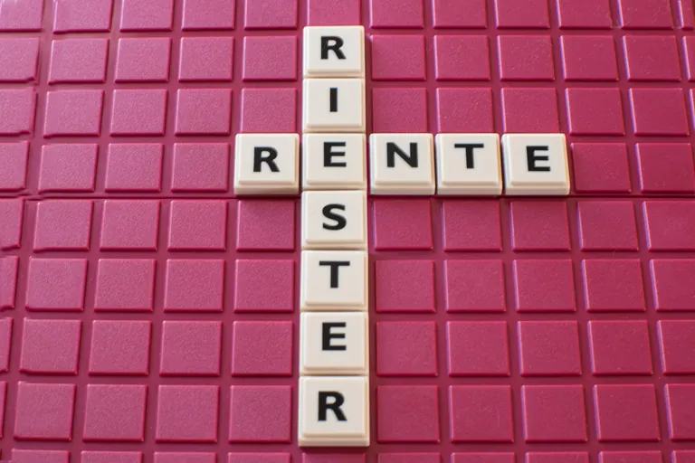 Wort "Riester-Rente" aus Spielsteinen auf rotem Spielbrett gelegt.