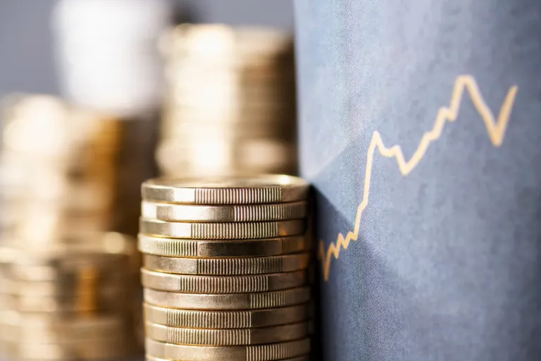 M&uuml;nzstapel vor Tafel mit aufsteigendem Graphen.