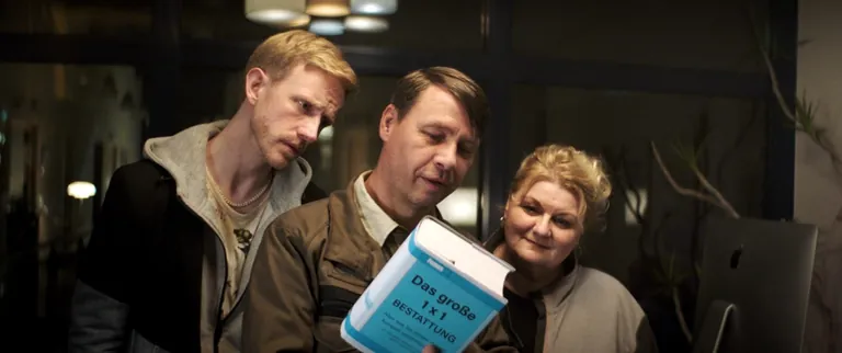 Szene aus "Wer begr&auml;bt den Bestatter?": Gert (Tom Kre&szlig;), Rudi (Angelika Sedlmeier) und Patrick (David Zimmerschied) machen sich mithilfe eines Buches schlau.