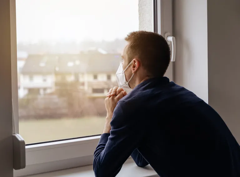 Mann mit FFP2-Maske schaut aus Fenster.