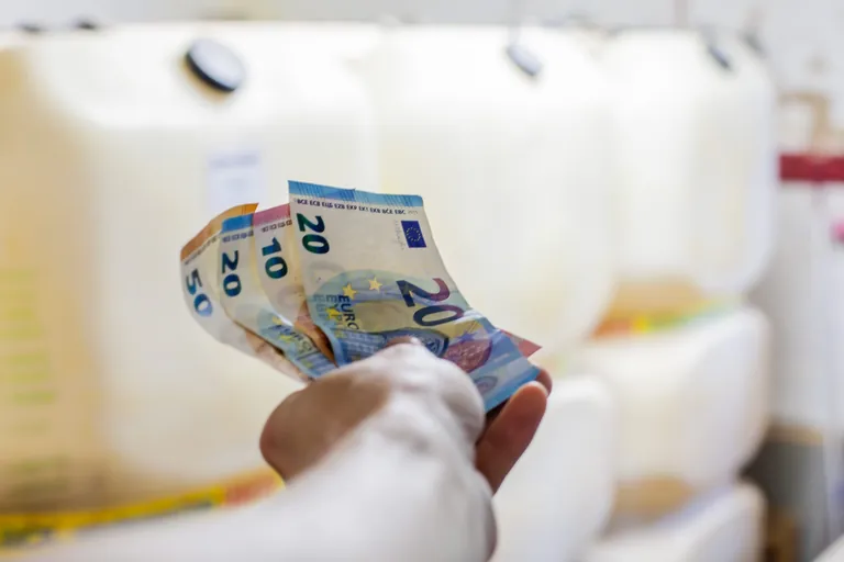 Hand h&auml;lt Geldscheine vor &Ouml;l-Kanister.