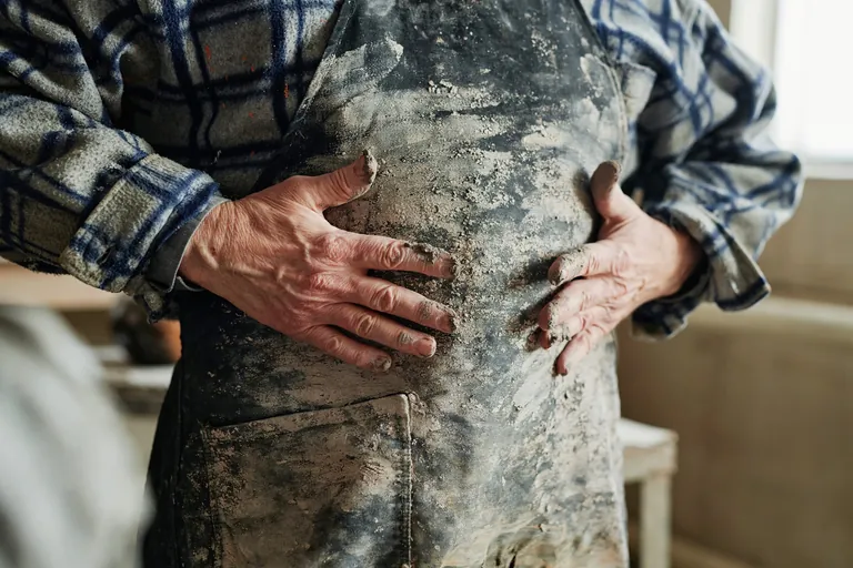 Handwerker schmiert sich Tonreste an Schürze ab.