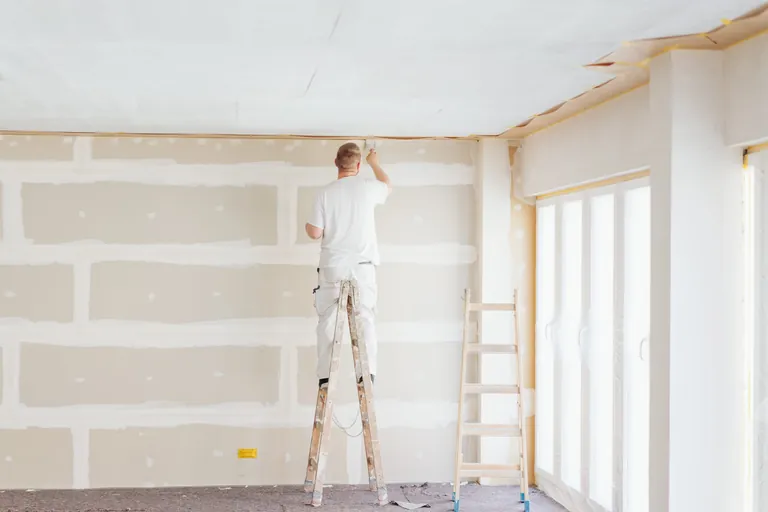 Maler steht auf Leiter und pinselt Wand.