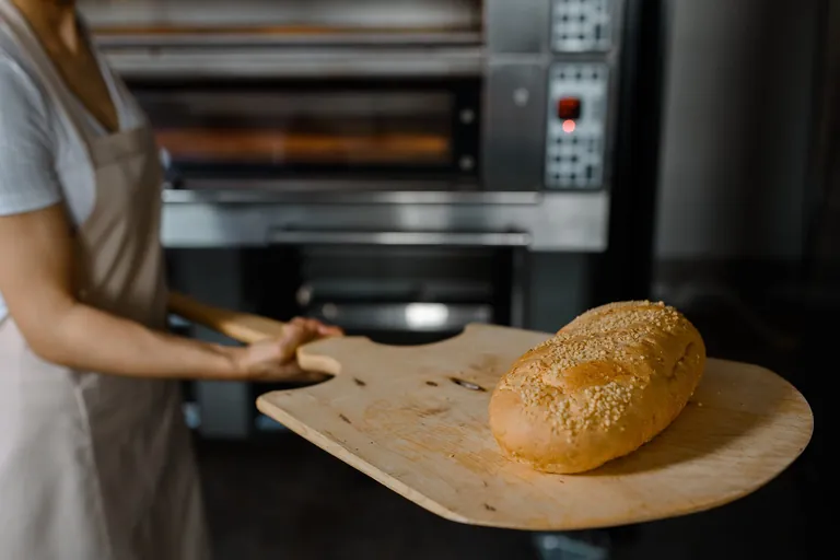 Nahansicht. Bäckerin schiebt Brot in Ofen.