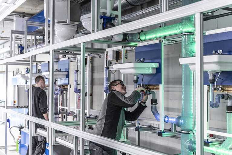 Zwei Auszubildende arbeiten an der Abwasserhydraulikwand im Bildungszentrum der SHK-Innung M&uuml;nchen.