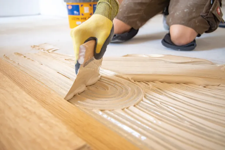 Bodenleger trägt Parkettkleber auf.