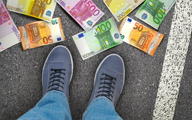 Geld liegt auf Stra&szlig;e. Turnschuhe stehen daneben.
