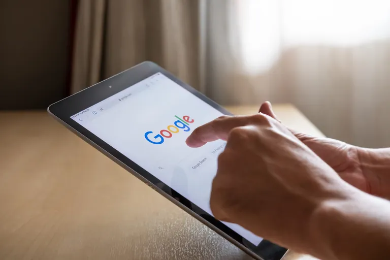 Hand tippt auf Tablet auf Google-Suchfeld.