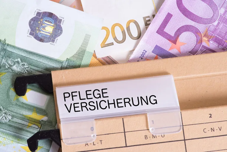 Euro-Geldscheine und eine Mappe mit Aufschrift "Pflegeversicherung".