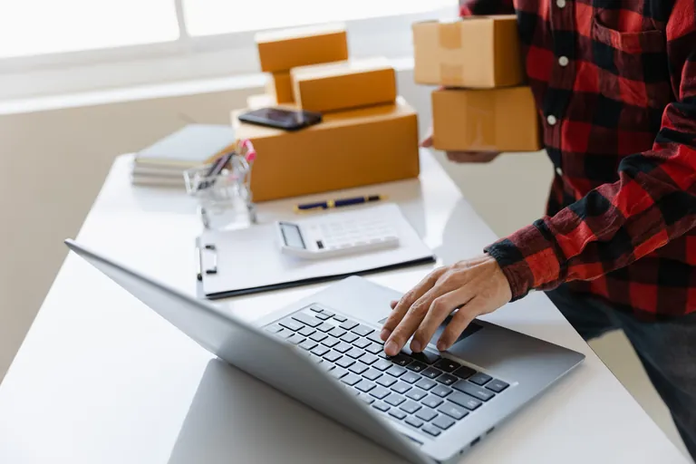 Mann mit Paketen in der Hand tippt auf Laptop.