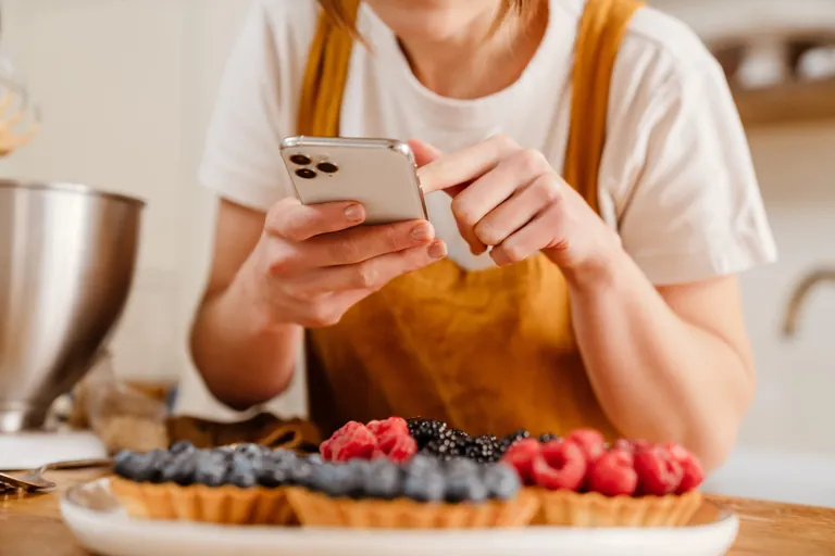 Eine junge B&auml;ckerin tippt auf ihrem Smartphone.