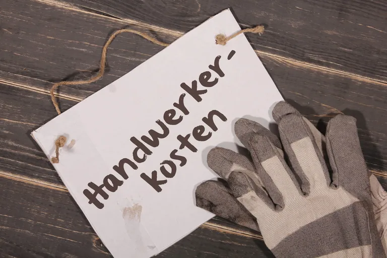 Bauhandschuhe und Schild mit Aufschrift "Handwerkerkosten".