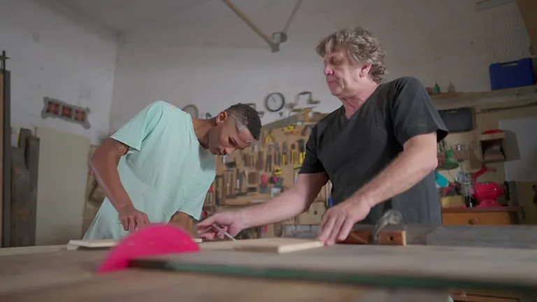 Einer Meister leitet seinen Lehrling im Tischlerhandwerk an.