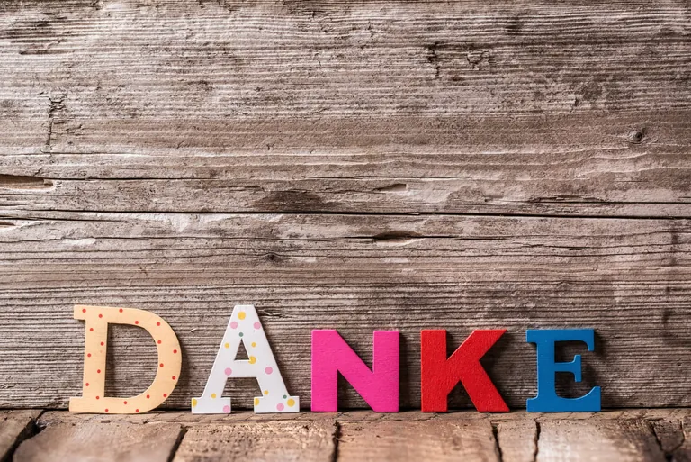 Bunte Buchstaben formen das Wort "Danke" vor hölzernem Hintergrund.