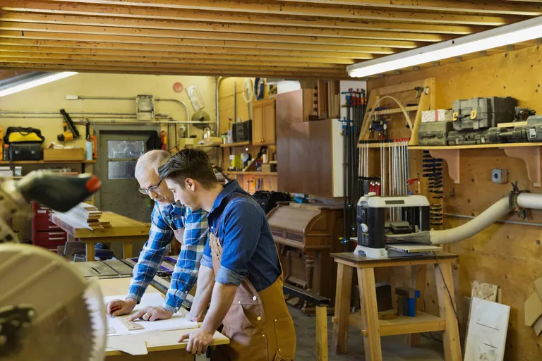 Schreiner und Auszubildender in Werkstatt.