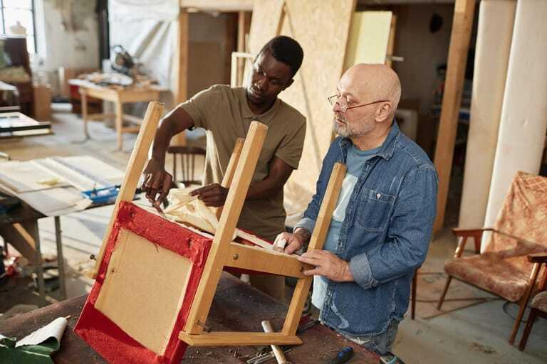 Zwei Handwerker reparieren einen Stuhl mit Polster.