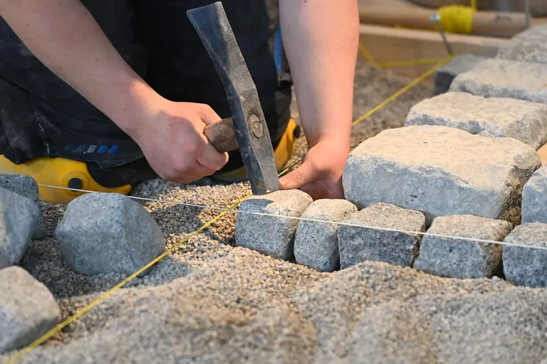 Ein Azubi verlegt Pflastersteine. 