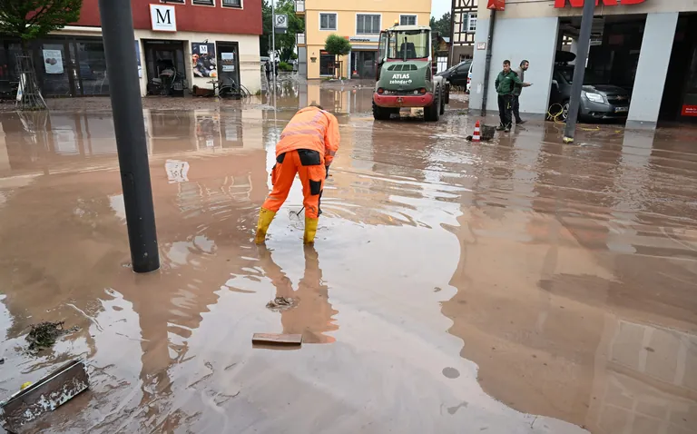 Auf einer nach einem Unwetter verschlammten Straße arbeitet ein Helfer. Seit Tagen kämpfen die Helfer in Bayern und Baden-Württemberg gegen die Flut und ihre Folgen.