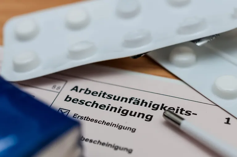 Tabletten und eine Arbeitsunf&auml;higkeitsbescheinigung liegen auf dem Tisch