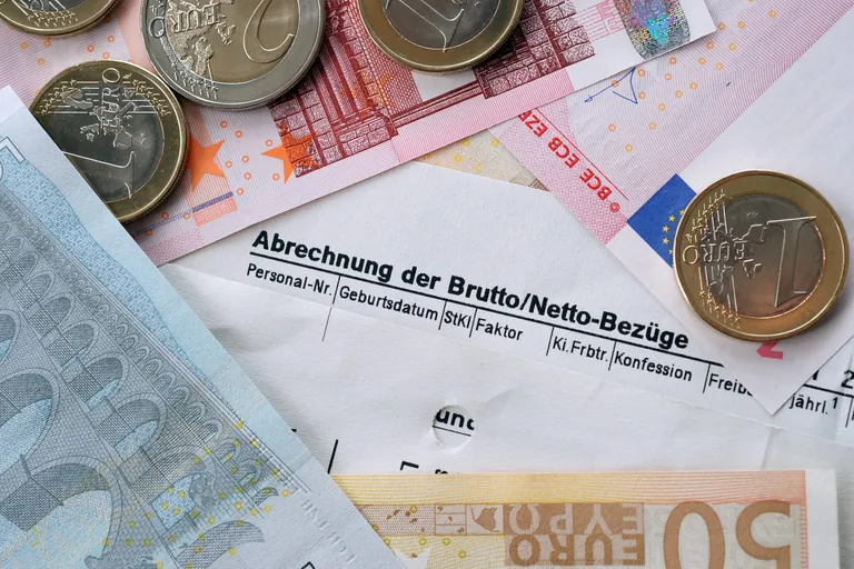 Geldscheine- und -münzen liegen auf einer Gehaltsabrechnung