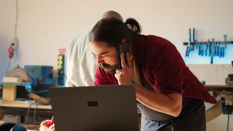 Schreiner, der einen Telefonanruf entgegennimmt, schreibt Informationen auf. Tischler in der Montagewerkstatt, Zeichnen von Schaltpl&auml;nen