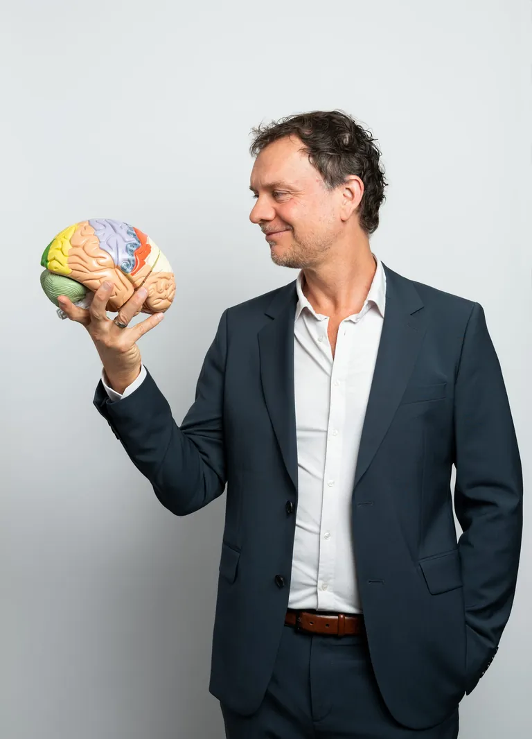 Prof. Dr. Volker Busch, Facharzt f&uuml;r Neurologie, &shy;Psychiatrie und Psychotherapie h&auml;lt ein Gehirmodell in der Hand und schaut es l&auml;chelnd an.